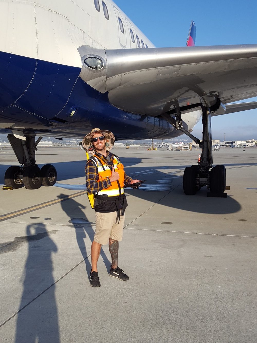 Kevin Foxcroft in a high-visibility vest and sun hat
                        holding a data collector beneath the wing of a parked
                        airliner.