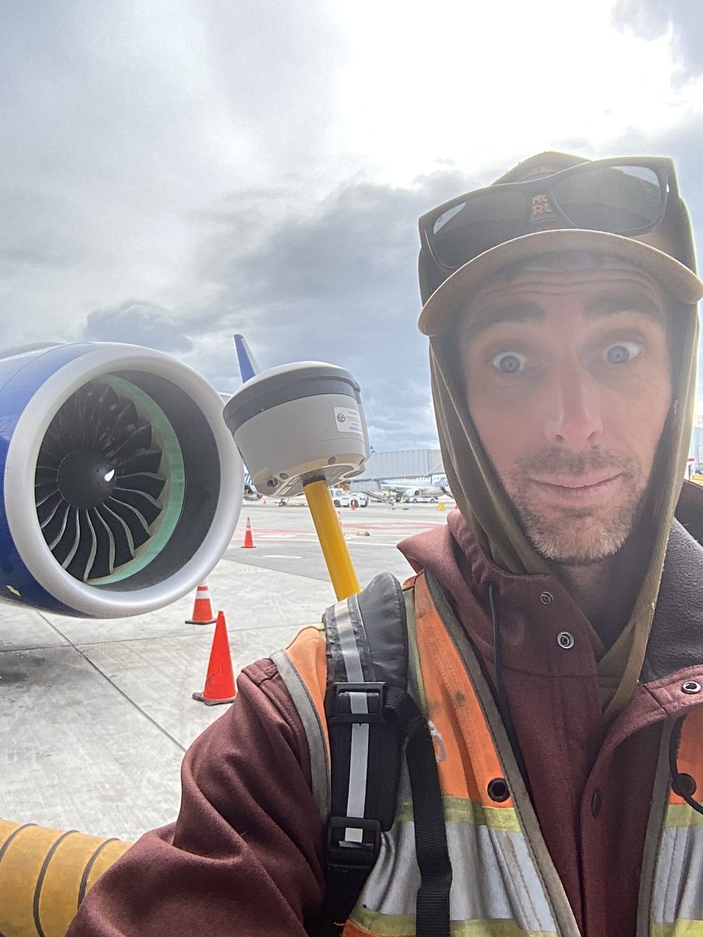 Kevin Foxcroft in a high-visibility vest holding a survey
                        pole with a GNSS receiver beside an aircraft engine on an
                        airport apron.